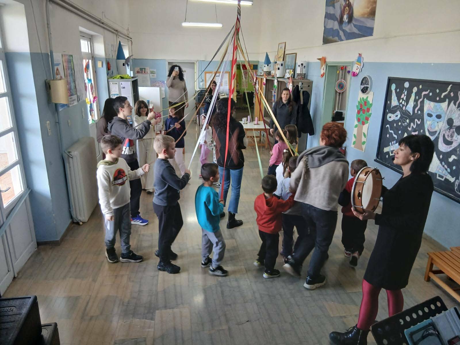 Παιδιά παίζουν γαϊτανάκι σε σχολική τάξη, με την Παναγιώτα Στραγανιώτη να παίζει ντέφι